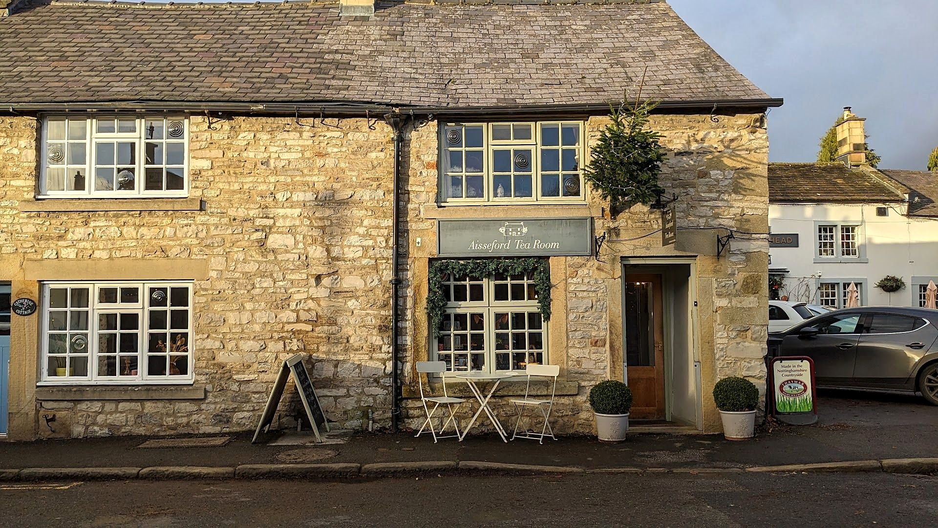 The Aisseford Tea Room: a low stone cottage on Church Street with white-framed windows, a hanging sign, a chalkboard by the door and small tables outside